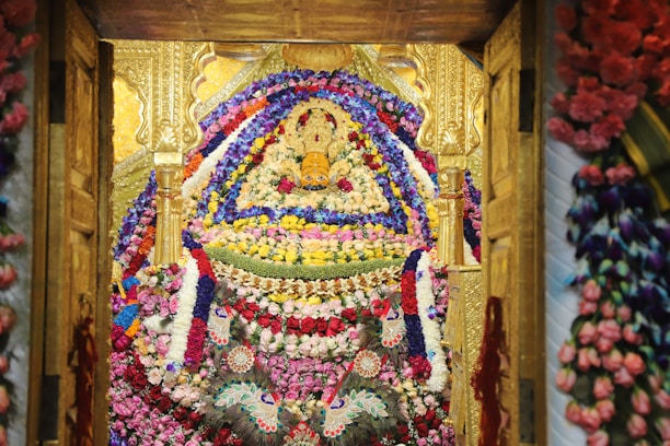 An elaborate floral arrangement adorns a richly decorated area with symmetrical patterns and detailed designs. The structure appears golden with intricate carvings, and the vast array of flowers includes pink, red, purple, and white tones, tightly packed together to form a visually stunning display.