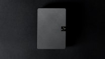 A rectangular object with diagonal stripe patterns is positioned against a dark background. The object has a small latch or button on one side, suggesting it might be a closed case or book-like item.
