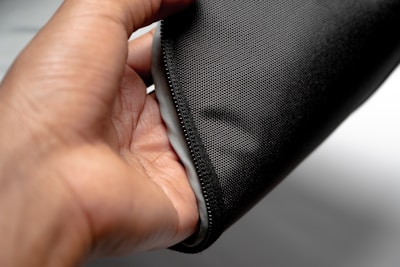 A hand holding a piece of soft, textured fabric that has a dark grey color. The fabric appears to be flexible and comfortable to touch, possibly used for clothing or upholstery.