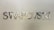 Metallic letters spelling 'SWAROVSKI' are mounted on a smooth, light-colored wall. The letters are reflective and have a shiny, polished finish.