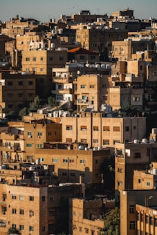 A dense cluster of beige and brown apartment buildings with flat roofs, many of which have water tanks and satellite dishes. The buildings are closely packed, creating a maze-like appearance. The sunlight casts shadows, adding depth and contrast to the urban landscape.