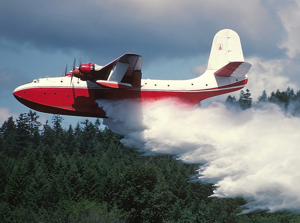 a red and white plane flying over a forest