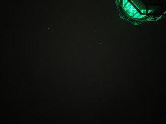 A dark sky with a faint presence of stars and a geometric, illuminated structure emitting green light in the upper right corner.