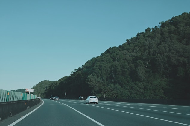 A convoy of cars traveling on a highway under a clear blue sky.