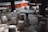 Stone tables and stools are arranged in an outdoor setting, surrounded by trees. The setting is shaded, with sunlight filtering through the leaves creating patterns on the ground. The furniture has a rustic and traditional design, likely made of granite or a similar material.