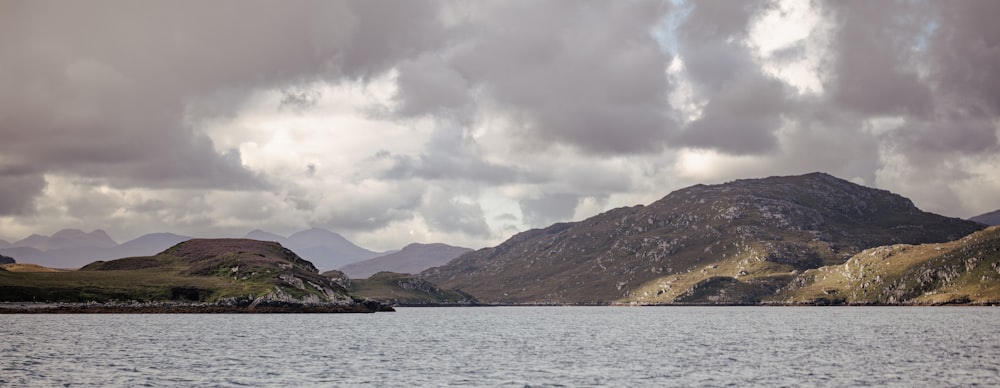 a body of water surrounded by mountains under a cloudy sky