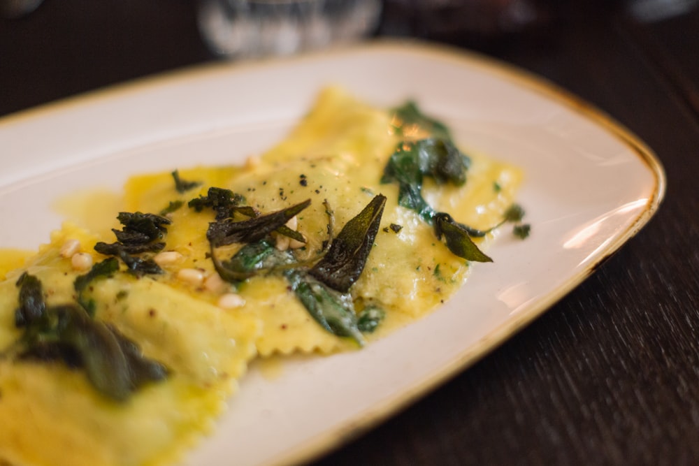 a white plate topped with ravioli covered in cheese and greens