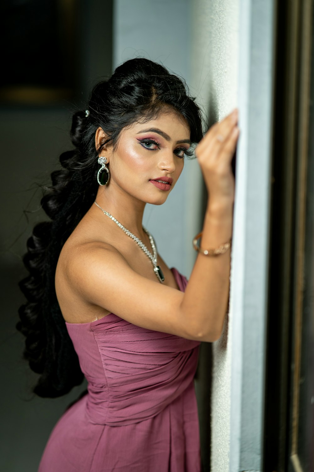 a woman in a purple dress leaning against a wall