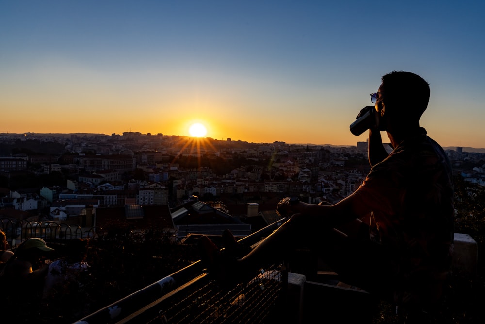 a man sitting on top of a metal railing next to a sunset