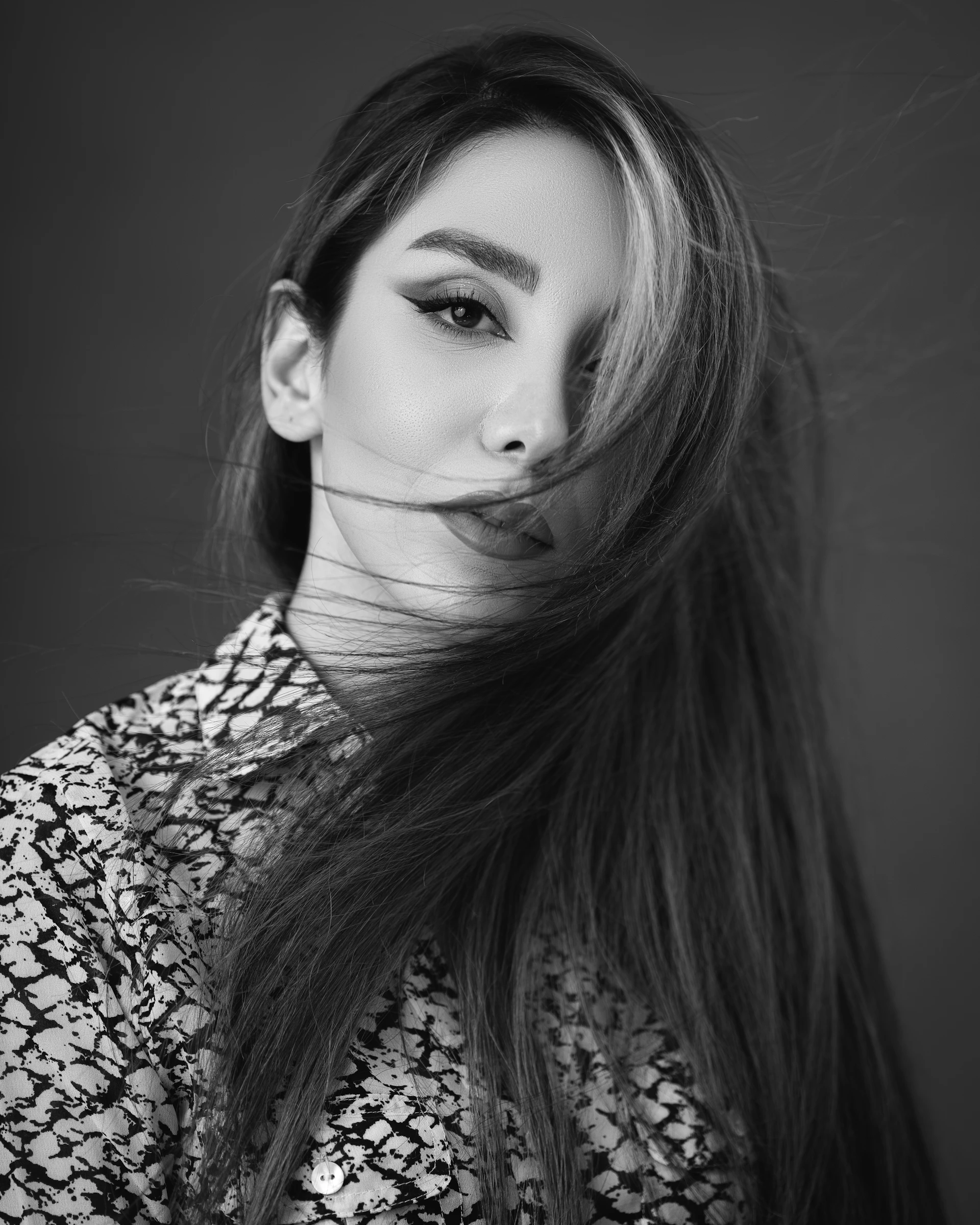A sultry black-and-white portrait of a woman draped in silk, her eyes inviting and mysterious against a softly lit backdrop.