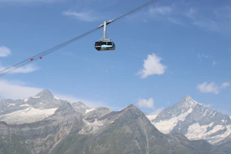 A colorful cable car ascending Shymbulak Mountain with snowy peaks in the background.