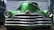 A vintage car with a shiny chrome grille and vibrant green paint. The car's rounded headlights and sleek design suggest a classic automobile aesthetic. It is parked in front of a corrugated metal garage with the shadow of another vehicle visible to the side.