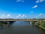 Construction workers laying concrete on a new bridge over a clear river.