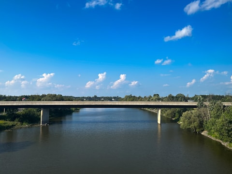A wide-angle view of a newly built concrete bridge spanning a river, with workers finishing final touches.