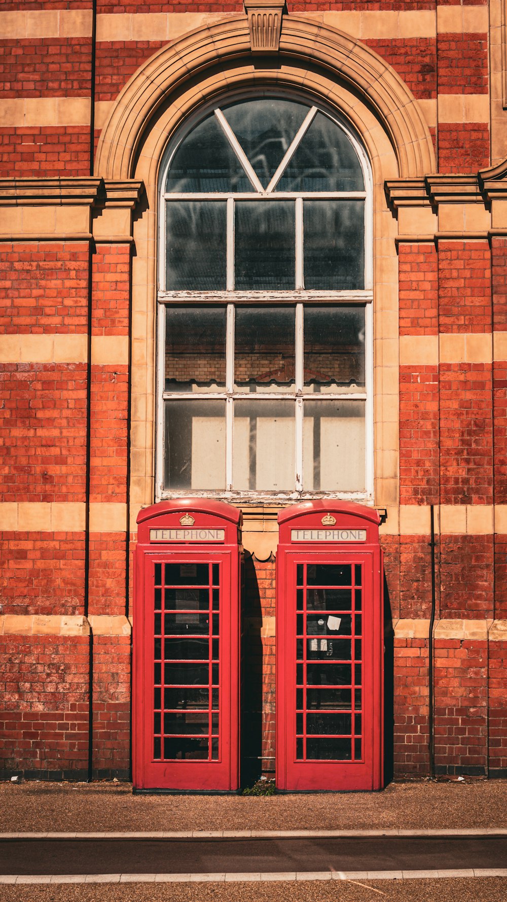 two red telephone booths in front of a brick building