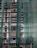 A building under construction is covered with green mesh fabric, with scaffolding visible behind it. The fabric appears to be draped unevenly, allowing glimpses of windows and the building's unfinished surfaces.