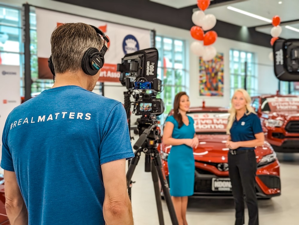 a man filming a woman in a car showroom