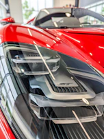 Close-up of a red sports car’s headlight and sleek curves under bright sunlight.