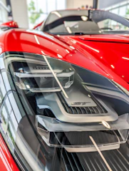 Close-up of a glossy red sports car hood reflecting garage lights.