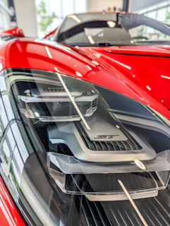 Close-up of a red sports car’s headlight and sleek curves under bright sunlight.