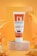 A tube of Dermalift Sunlift tinted sunscreen cream with SPF 50 is displayed. The tube is placed on a marble-like pedestal and has a vibrant orange and white design. The background features tropical palm leaves and an orange gradient, creating a warm, summer ambiance.