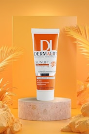 A tube of Dermalift Sunlift tinted sunscreen cream with SPF 50 is displayed. The tube is placed on a marble-like pedestal and has a vibrant orange and white design. The background features tropical palm leaves and an orange gradient, creating a warm, summer ambiance.