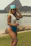 A stylish woman wearing a sleek Pacific Blue swimsuit standing by a sunlit beach cabana.