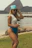 A stylish woman wearing a sleek Pacific Blue swimsuit standing by a sunlit beach cabana.