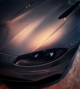 Close-up of a gleaming exotic car hood reflecting soft blue lighting in a sleek black and white studio.