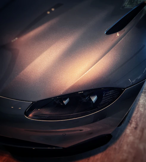Close-up of a glossy black sports car hood reflecting golden light accents.