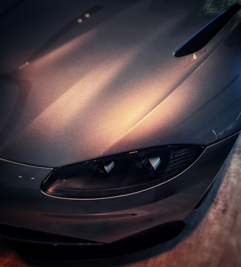 Close-up of a gleaming exotic car hood reflecting soft blue lighting in a sleek black and white studio.