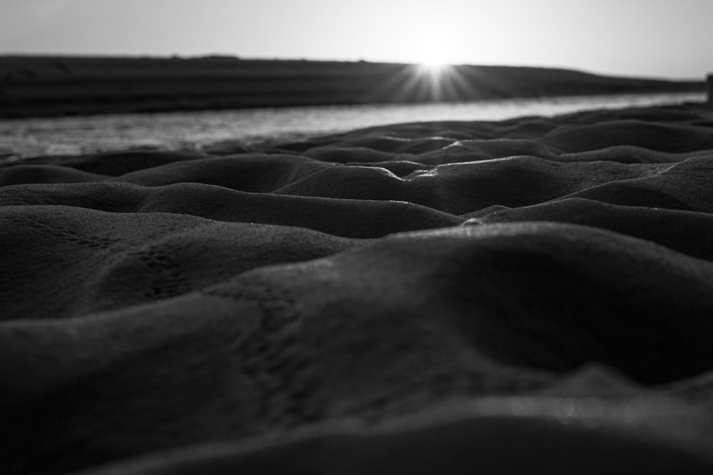 a black and white photo of the sun setting over a beach