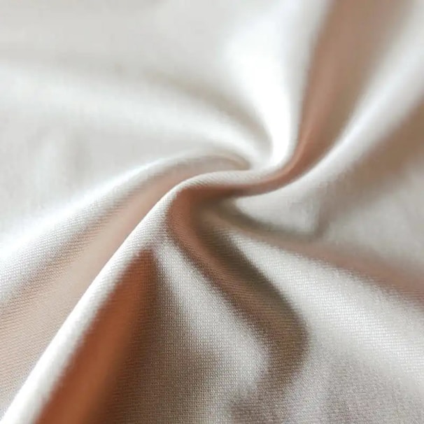 Close-up of soft, flowing fabric in a warm neutral tone, highlighting the texture and quality of the material.