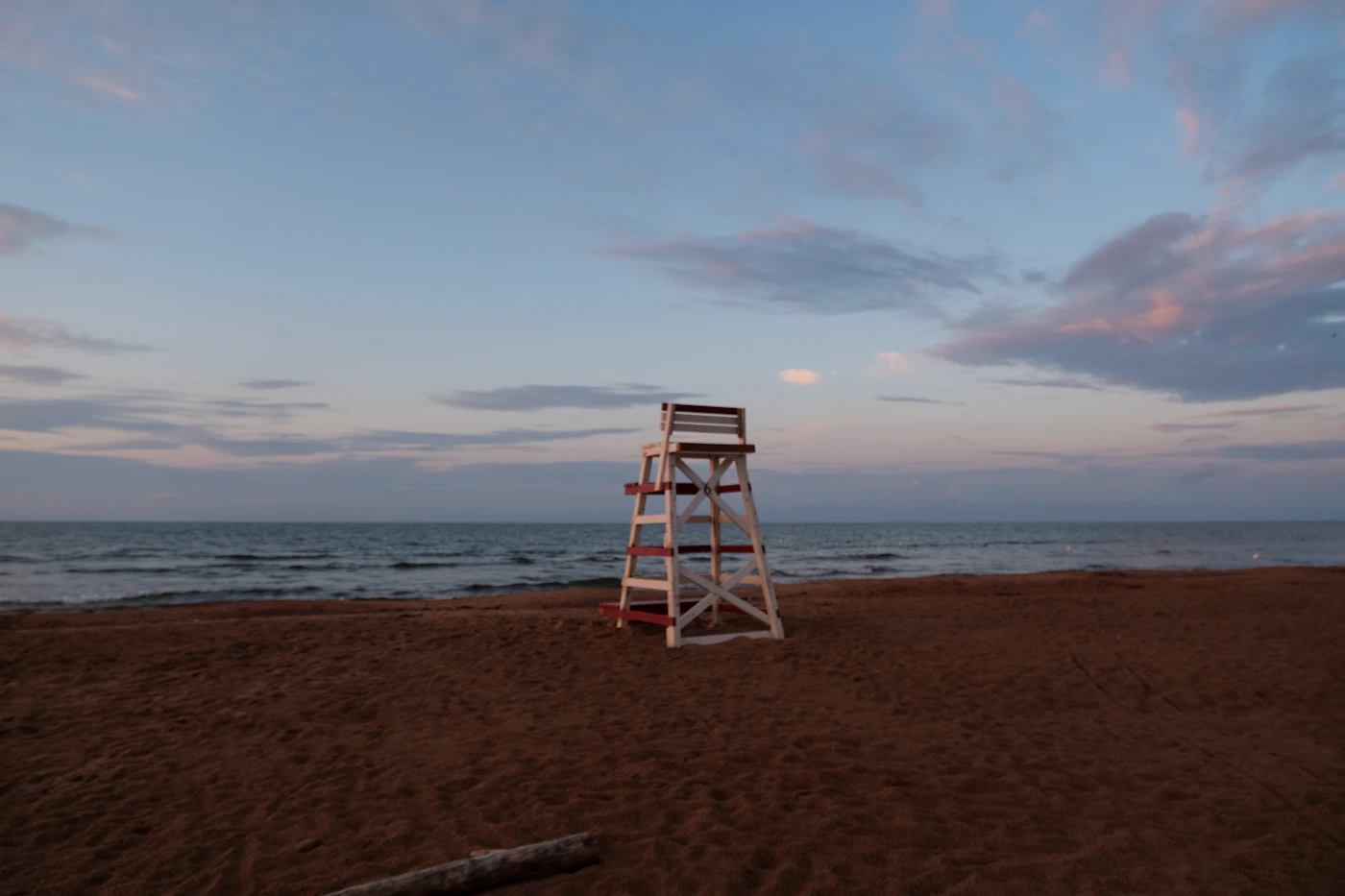 PEI red sand beach at dusk with a lifeguard stand silhouetted against a pastel pink and blue sky, light surf on the red shore