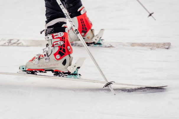Close-up of ski boots and poles resting on fresh snow beside a frozen lake.
