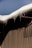 A sloped roof covered with a thick layer of snow, with icicles hanging from the edge. The building has a corrugated metal wall creating a distinct shadow pattern.