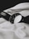 A classic analog wristwatch with a dark leather strap lies on a textured white fabric. The watch face is black with minimalist numbering, reflecting a simple yet elegant design.