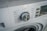 A close-up view of a washing machine control panel with various washing options such as Speed Wash, Cotton, Synthetic, and others. The dial knob is prominently positioned, slightly tilted to the left. Adjacent buttons display functions like Delay and Temperature.