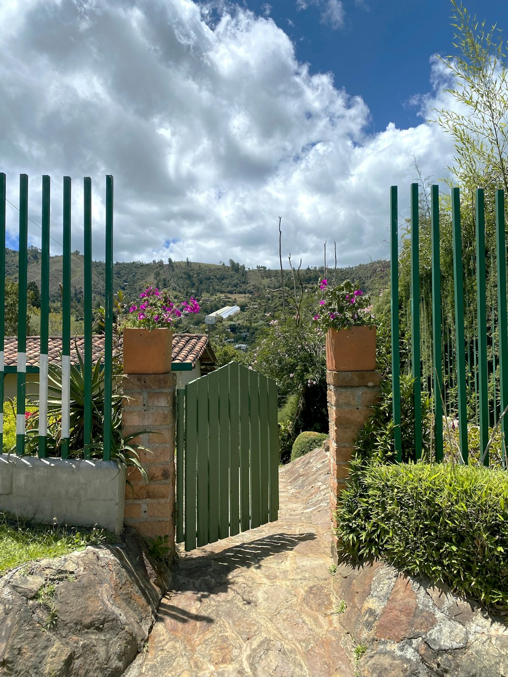 a green gate is open on a stone path