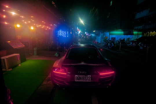 A sleek pink car driving through a modern city street at night with soft glowing lights.