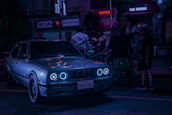 A group of passionate car enthusiasts gathered around a modified car, sharing stories under dim streetlights.