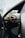 A luxurious car interior featuring a sleek black leather seat and a steering wheel with red accents. The dashboard includes digital displays and a high-tech control panel. The view through the open car door reveals a glimpse of blurred greenery outside.