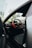 A luxurious car interior featuring a sleek black leather seat and a steering wheel with red accents. The dashboard includes digital displays and a high-tech control panel. The view through the open car door reveals a glimpse of blurred greenery outside.