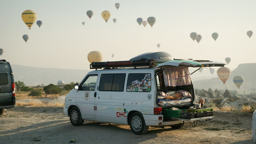 a van is parked in a field with hot air balloons in the sky
