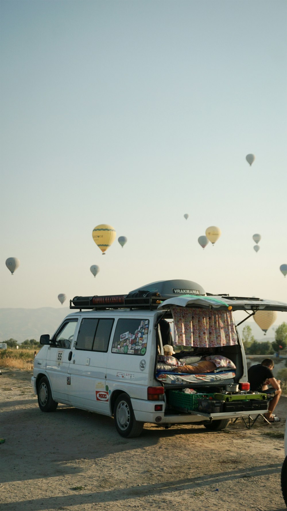 a van parked in a field with hot air balloons flying in the sky