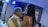 An older man and a younger woman are sharing a dance at what seems to be a social gathering or celebration. The man is smiling warmly, and the woman has her arms around his shoulders. The setting appears intimate with dim lighting and a soft blue glow from overhead lights.