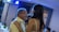 An older man and a younger woman are sharing a dance at what seems to be a social gathering or celebration. The man is smiling warmly, and the woman has her arms around his shoulders. The setting appears intimate with dim lighting and a soft blue glow from overhead lights.