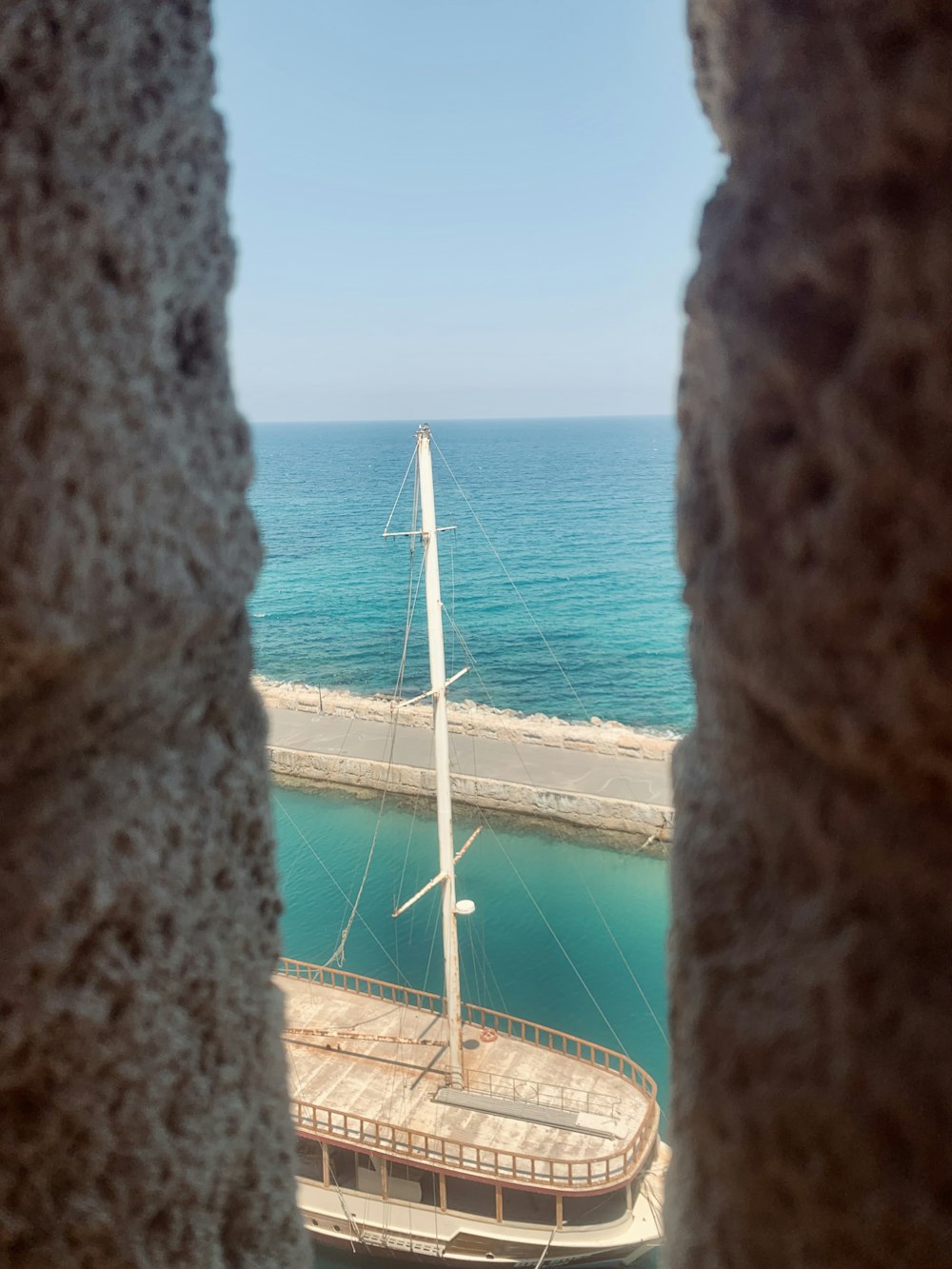 a view of a sailboat from a window in a stone wall