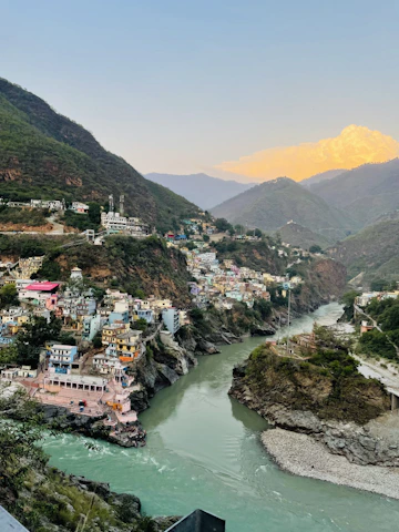 A stunning panoramic view of a colorful Latin American village embracing mountains and a sparkling river at sunset.