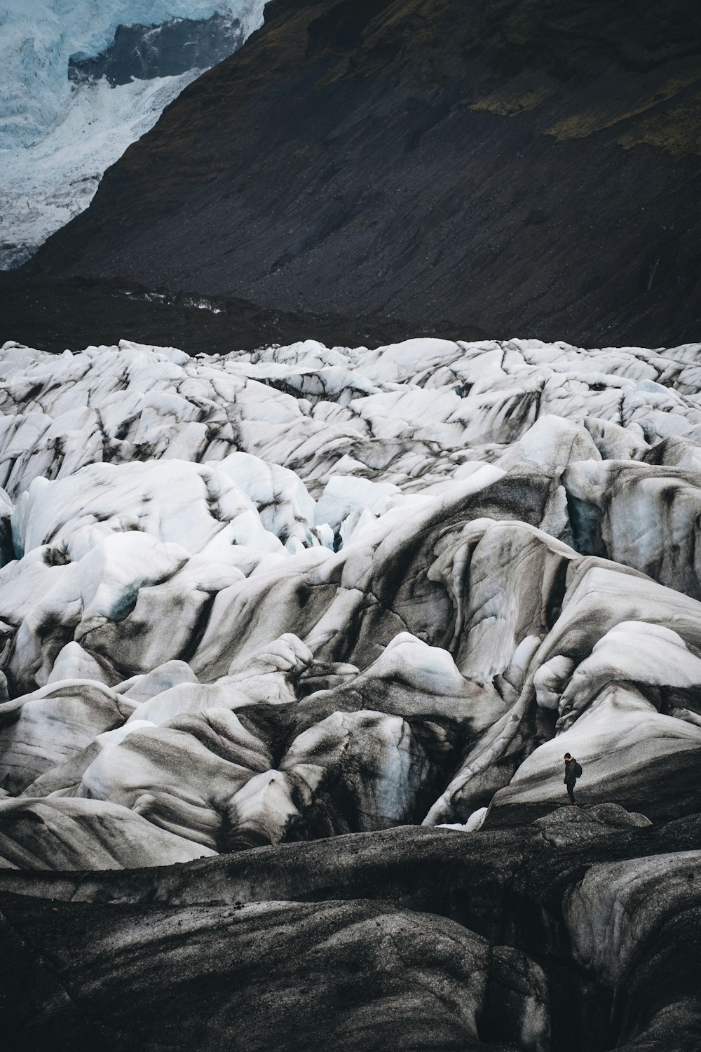 a man standing on top of a glacier next to a mountain